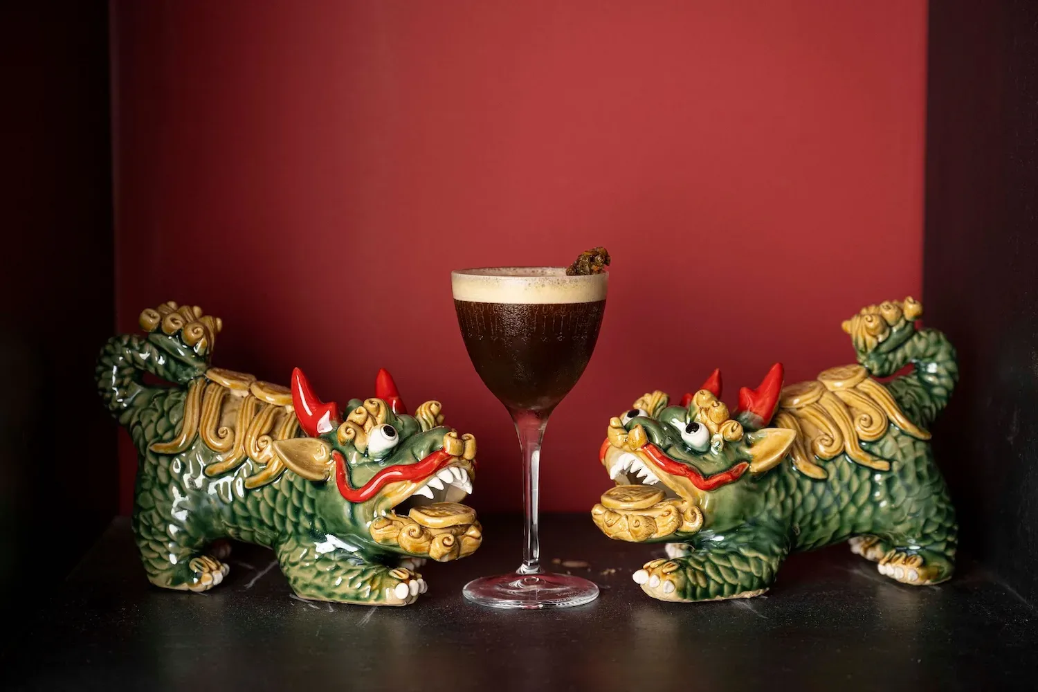 A signature cocktail flanked by foo dog statues at Madame Claude